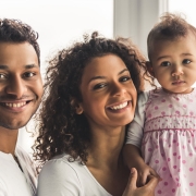A man and woman smile at the camera while holding a young child in a pink polka dot dress, capturing a joyful moment in the bright office of friendly orthodontists.